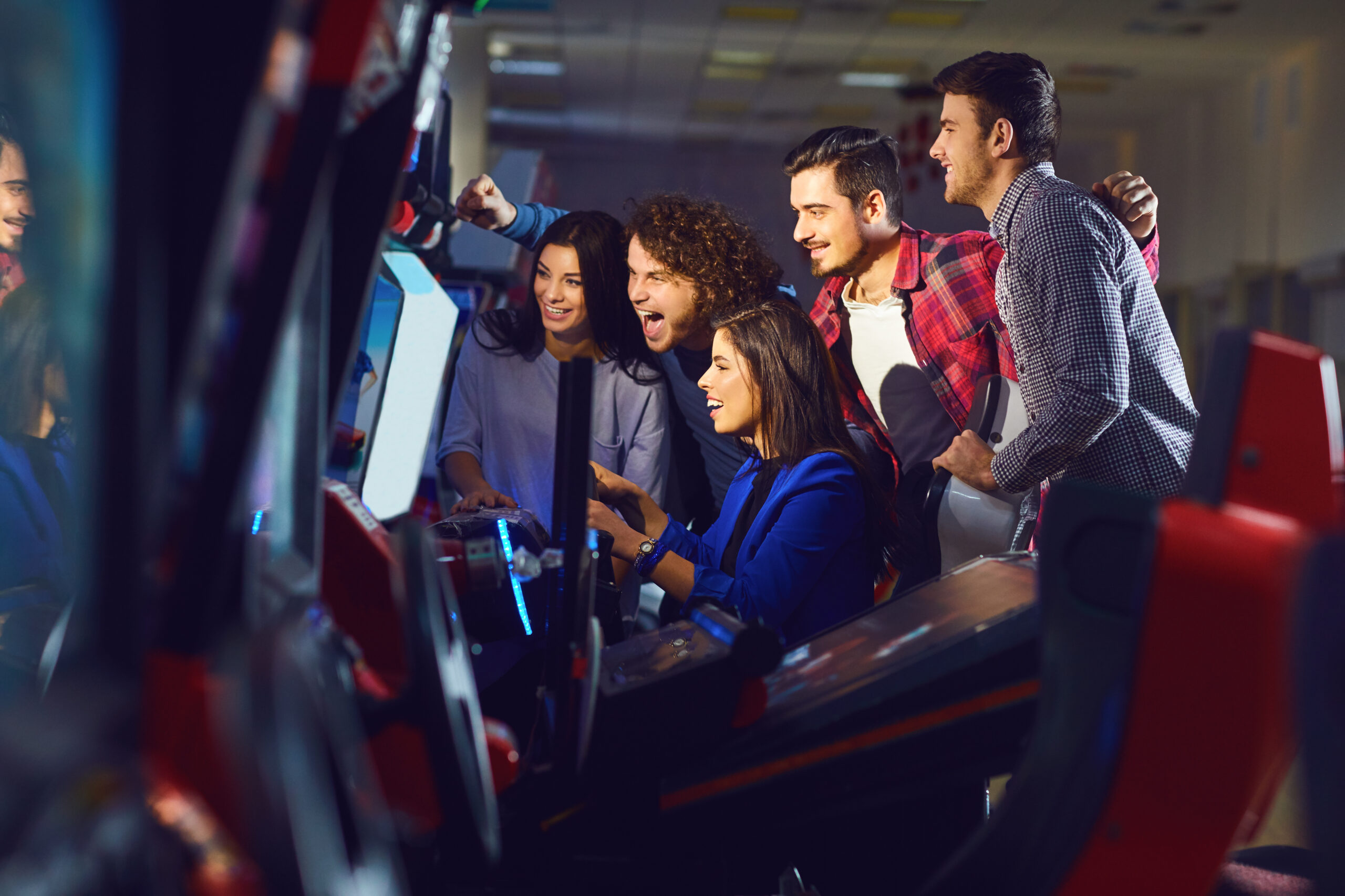 A group of friends playing arcade machine. in an amusement park. Young people have fun.